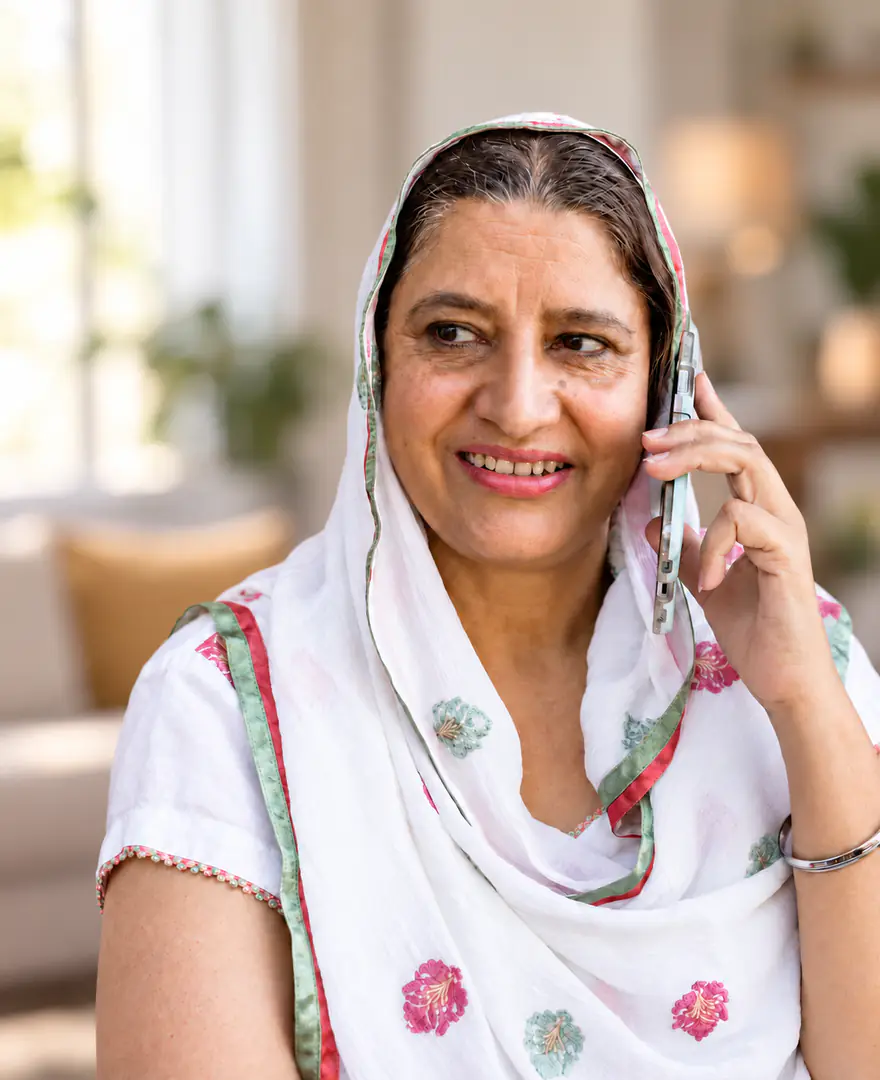 An older woman in a white dupatta smiling as she talks on her phone